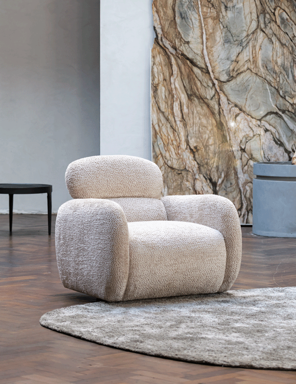 XOOON Ostia fauteuil op vloerkleed voor marmeren wand en ronde plantenbak in lichte moderne woonkamer