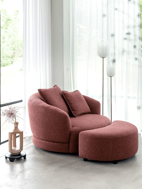 Rode XOOON Cervos fauteuil met twee kussens en bijpassende halfronde hocker in lichte ruimte met gordijnen en staande lampen