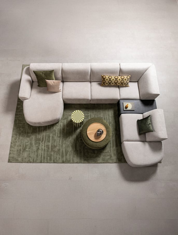 Modulares Sofa mit Chaiselongue in hellem Stoff, Zierkissen in warmen Tönen auf braunem Teppich mit drei runden Couchtischen von XOOON