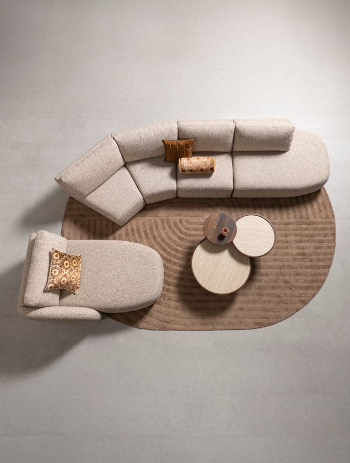 L-förmiges modulares Sofa in hellem Stoff mit Zierkissen auf grünem Teppich und runden Couchtischen von XOOON