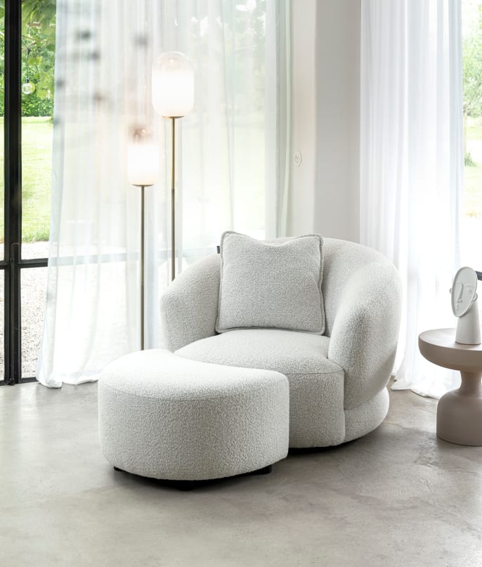 Witte XOOON Cervos fauteuil met kussen en bijpassende halfronde hocker in lichte ruimte met gordijnen en staande lampen